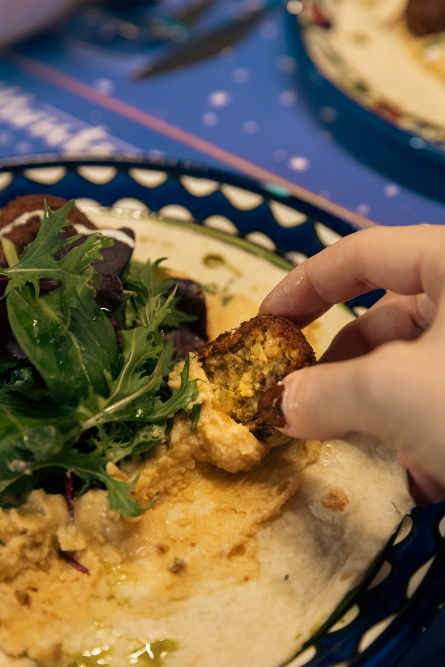 Gost uzima falafel sa tanjira sa humusom i salatom